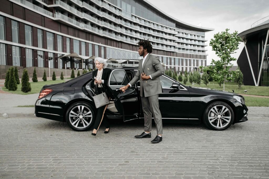 Chauffeur opening the rear door of a black sedan for a passenger